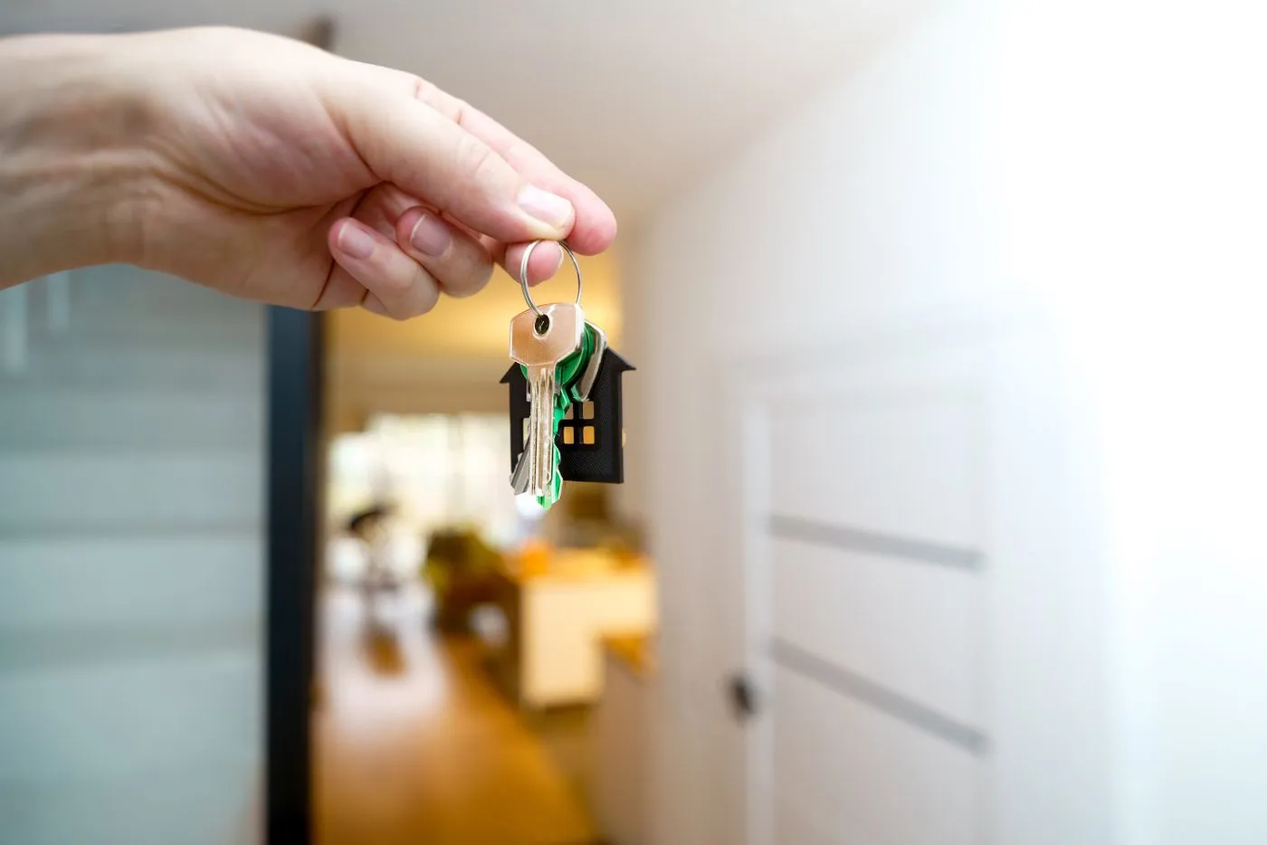 Hand holding house keys with a house keyring in a doorway