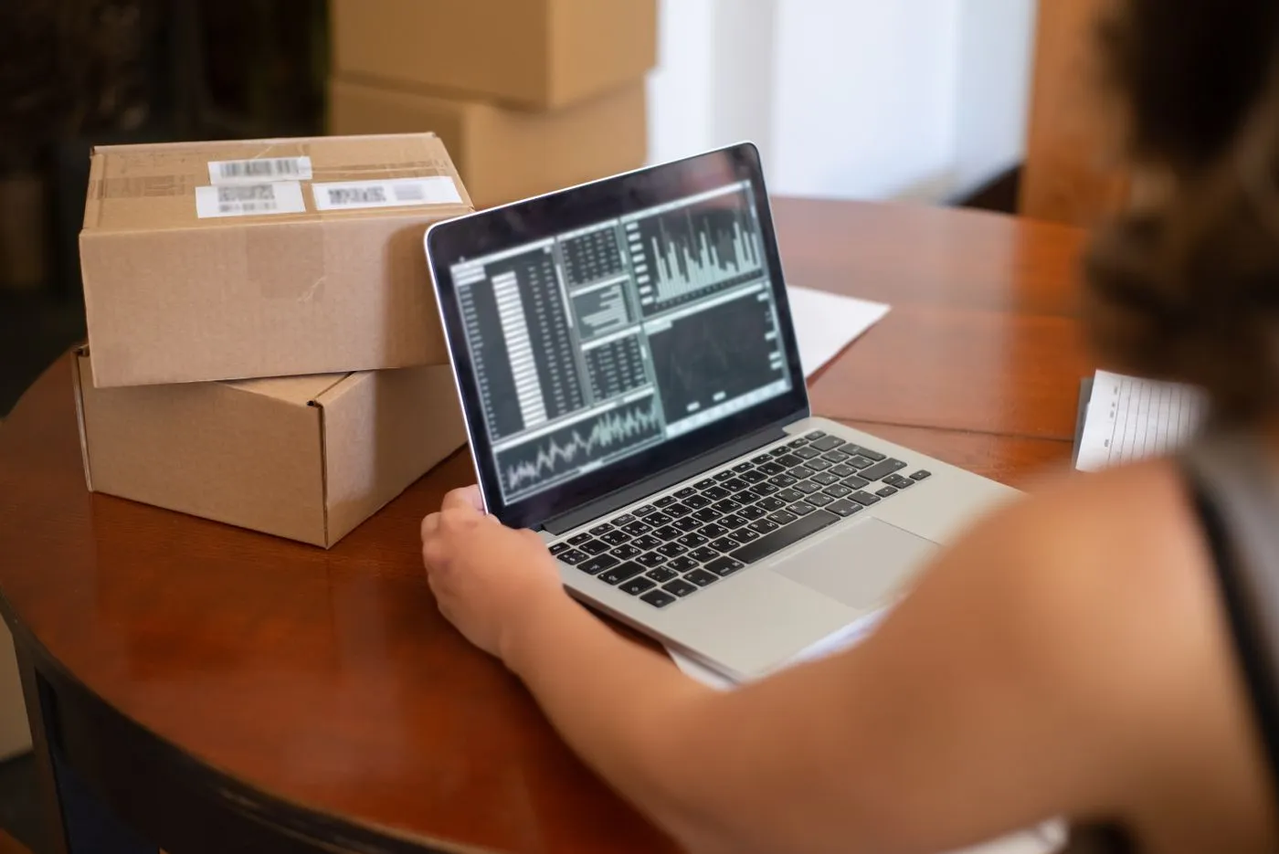 Small business owner reviewing charts on a laptop beside shipping boxes
