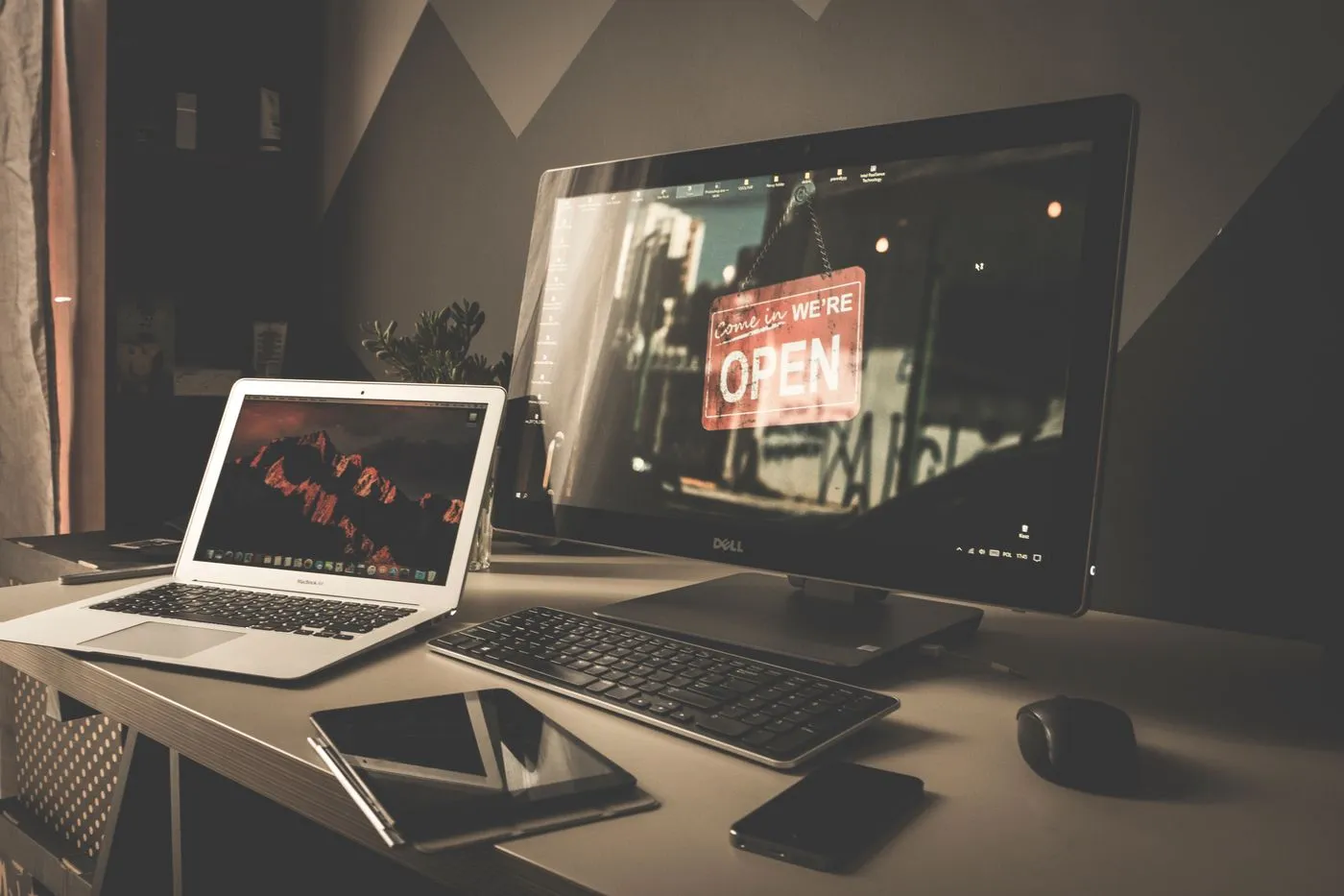Desktop and laptop workspace with a small business open sign on screen