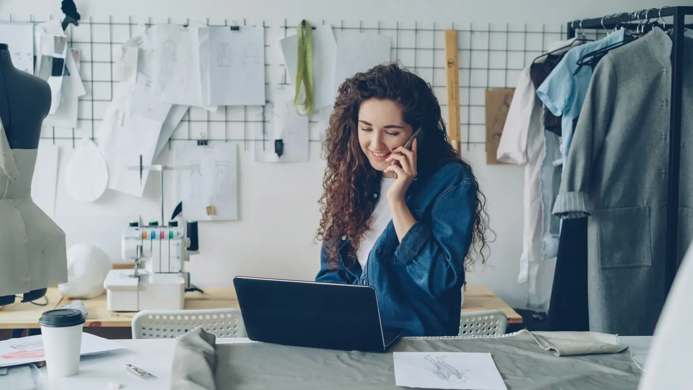 A small business owner in her studio, smiling on a phone call next to her laptop