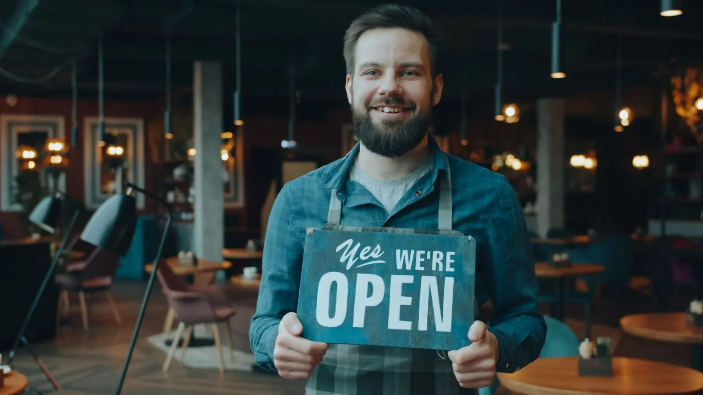 A cafe owner holding a sign that says Yes, we're open